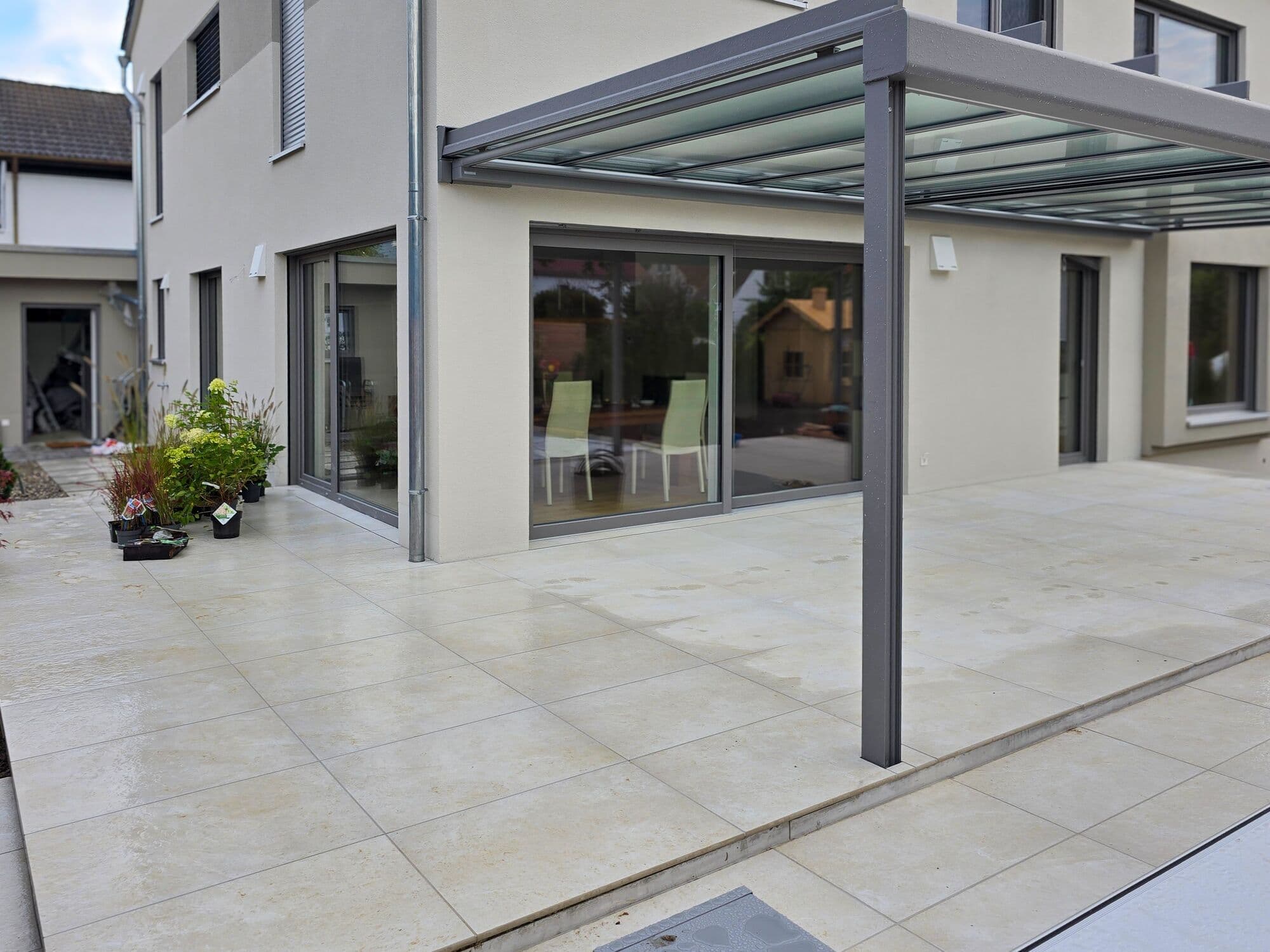 Terrasse aus hellen Großformatplatten mit Pergola am Haus